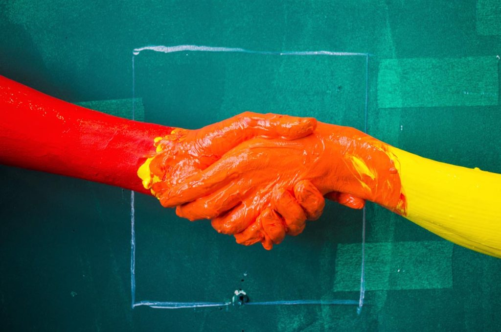 Two hands covered in paint against a green painted wall