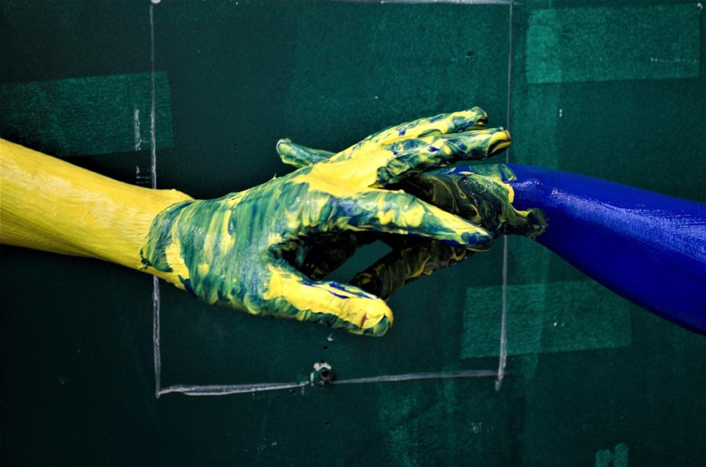 Two hands covered in paint against a green painted wall