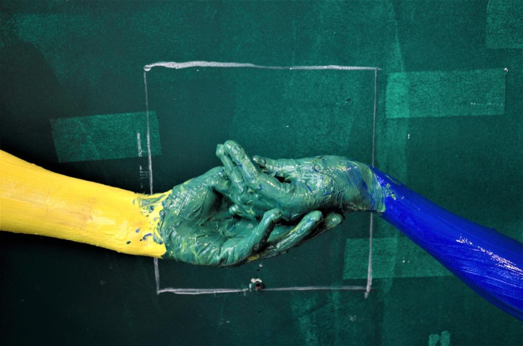 Two hands covered in paint against a green painted wall