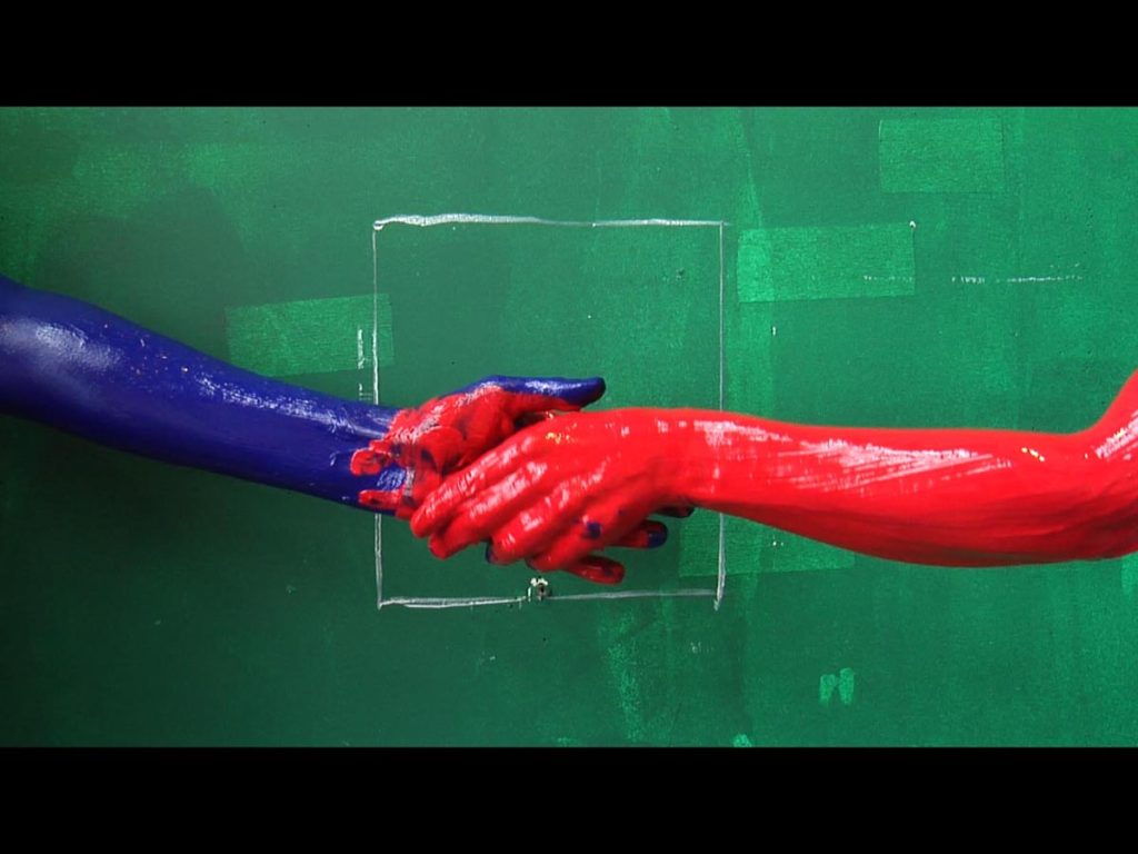 Two hands covered in paint against a green painted wall