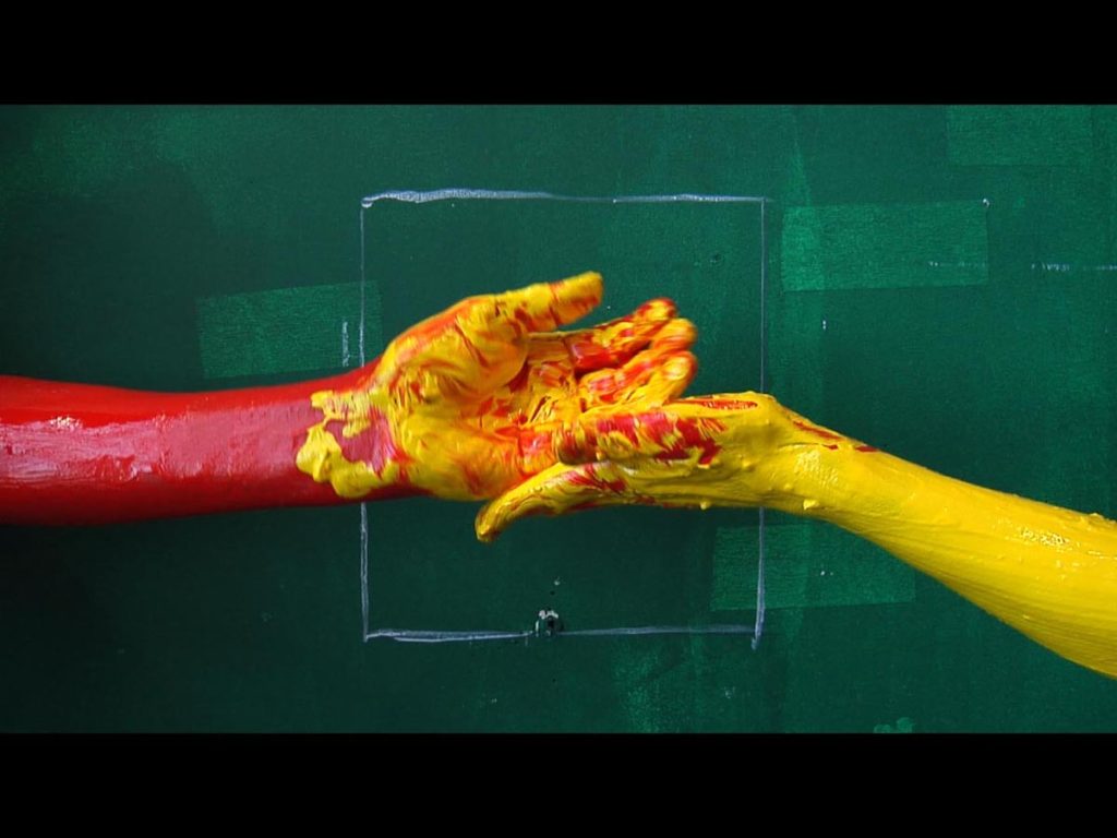 Two hands covered in paint against a green painted wall