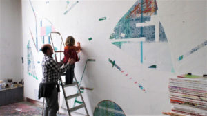 A man and a child sticking artwork to a studio wall