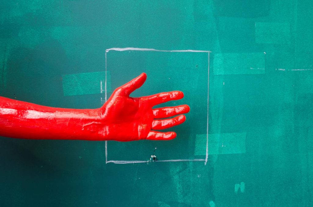 A hand covered in paint against a green painted wall