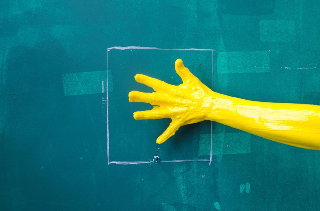 A hand covered in paint against a green painted wall