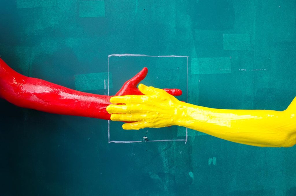 Two hand covered in paint against a green painted wall