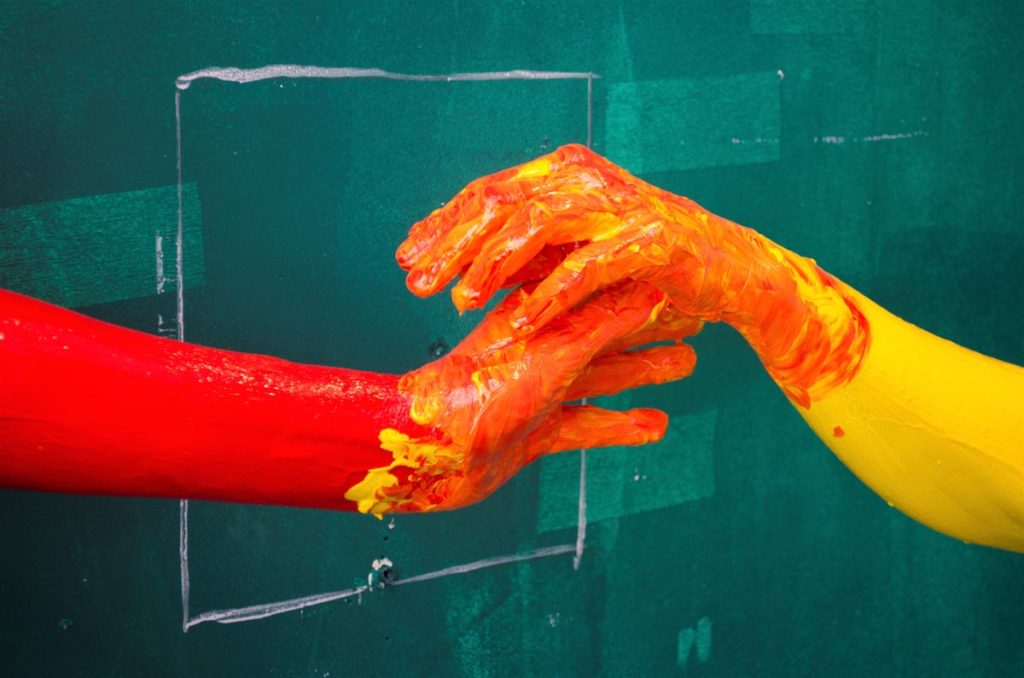 Two hand covered in paint against a green painted wall