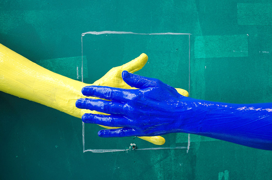 Two hands covered in paint against a green painted wall