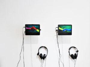 An art installation with two video screens and two sets of headphones on a white wall